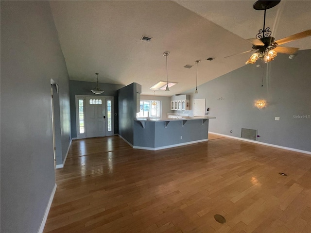 kitchen with kitchen peninsula, ceiling fan, a breakfast bar, wood-type flooring, and pendant lighting