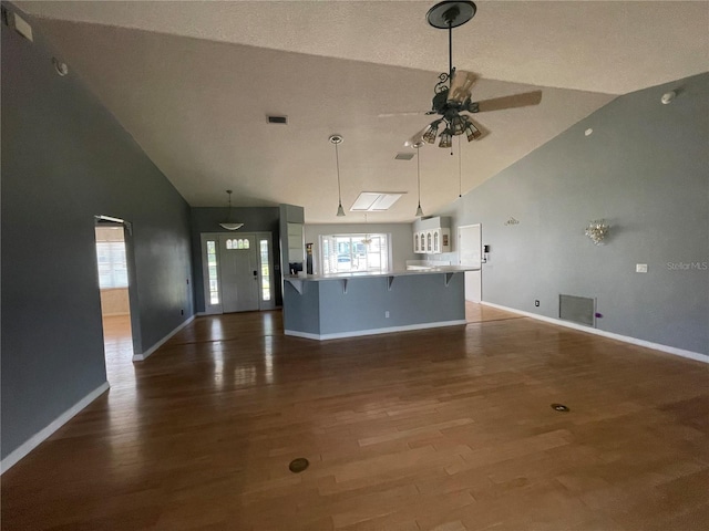 unfurnished living room with a ceiling fan, visible vents, baseboards, and wood finished floors