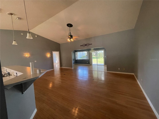 unfurnished living room with dark wood-type flooring, ceiling fan, high vaulted ceiling, and baseboards