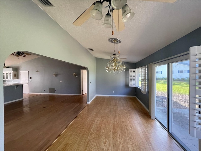 unfurnished dining area with wood finished floors, visible vents, vaulted ceiling, and ceiling fan with notable chandelier