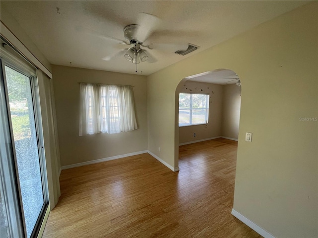 unfurnished room featuring arched walkways, visible vents, ceiling fan, and light wood-style flooring