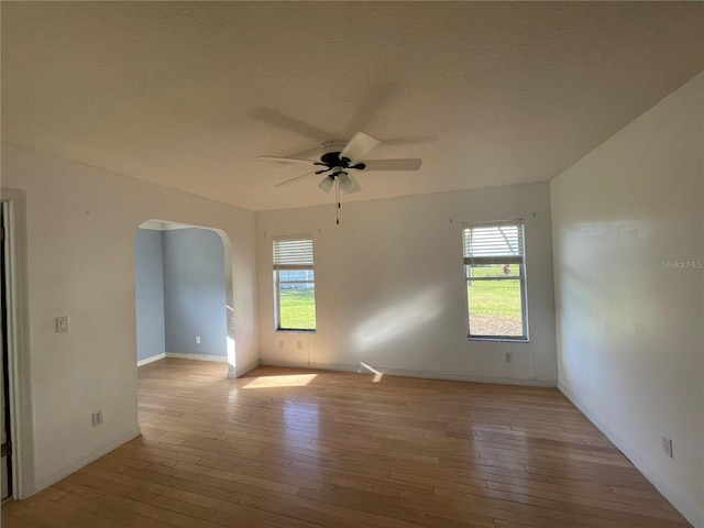 unfurnished room with light wood-style floors, ceiling fan, arched walkways, and a textured ceiling