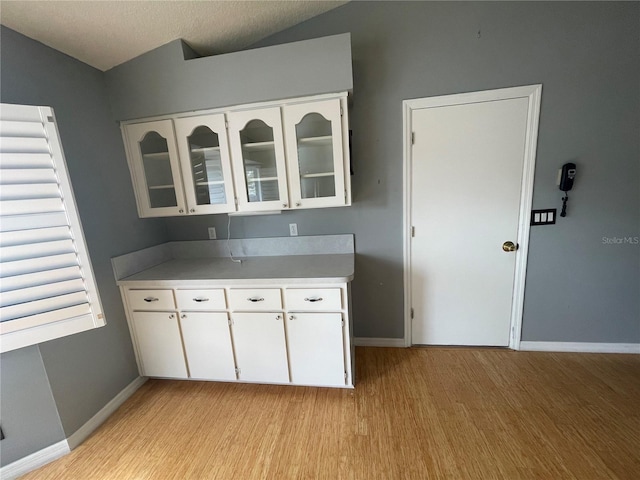 kitchen featuring lofted ceiling, light countertops, glass insert cabinets, light wood-style floors, and white cabinetry