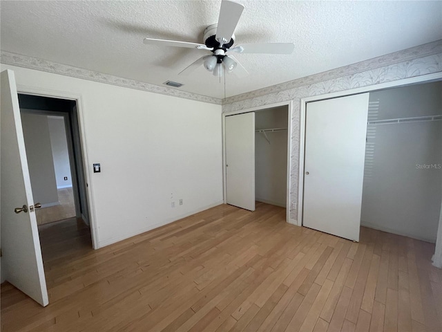 unfurnished bedroom with a textured ceiling, light wood-style flooring, visible vents, a ceiling fan, and two closets