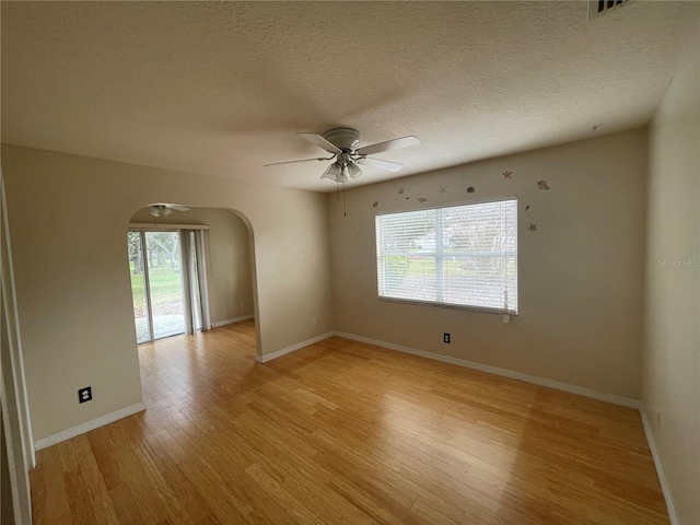 empty room with arched walkways, ceiling fan, baseboards, and light wood-style floors