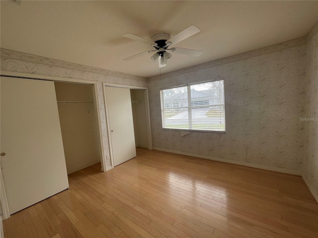 unfurnished bedroom with light wood finished floors, multiple closets, and wallpapered walls