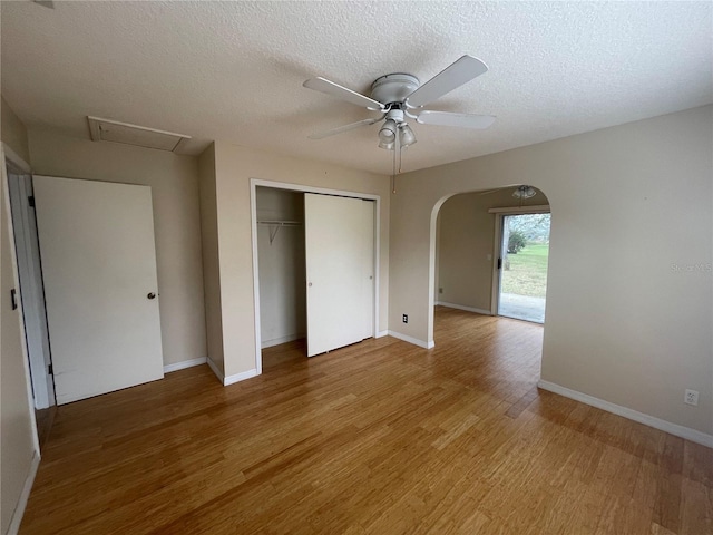 unfurnished bedroom with arched walkways, a closet, a textured ceiling, wood finished floors, and baseboards