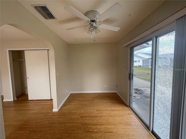 spare room featuring arched walkways, visible vents, light wood-style floors, ceiling fan, and baseboards