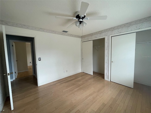 unfurnished bedroom featuring visible vents, ceiling fan, a textured ceiling, light wood-type flooring, and two closets