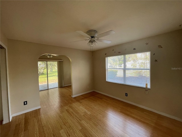 unfurnished room featuring arched walkways, light wood finished floors, a ceiling fan, and baseboards