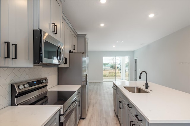 kitchen with appliances with stainless steel finishes, tasteful backsplash, sink, gray cabinets, and an island with sink