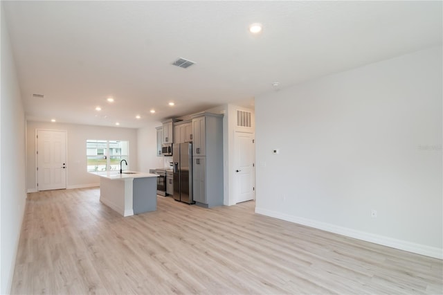 kitchen with gray cabinetry, sink, stainless steel appliances, light hardwood / wood-style floors, and a center island with sink