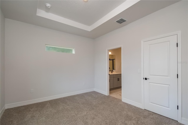 unfurnished bedroom with a raised ceiling, connected bathroom, and light colored carpet