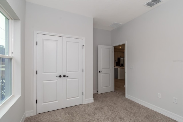 unfurnished bedroom with stainless steel fridge, light colored carpet, and a closet