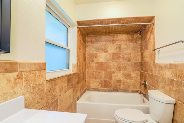 bathroom featuring toilet, tiled shower / bath, and tile walls