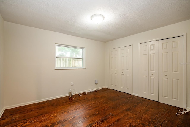 unfurnished bedroom with dark hardwood / wood-style floors, two closets, and a textured ceiling