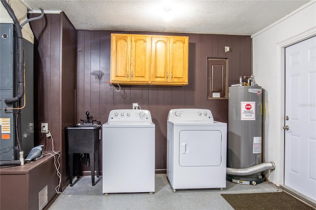 washroom with water heater, cabinets, a textured ceiling, washing machine and clothes dryer, and wood walls