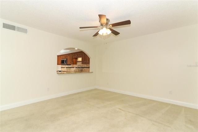 empty room with sink, ceiling fan, light colored carpet, and a textured ceiling