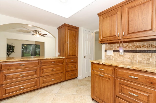 kitchen with decorative backsplash, light tile patterned floors, light stone counters, and ceiling fan