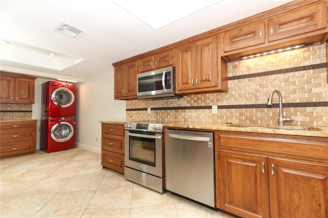 kitchen with tasteful backsplash, sink, stacked washer and clothes dryer, and appliances with stainless steel finishes