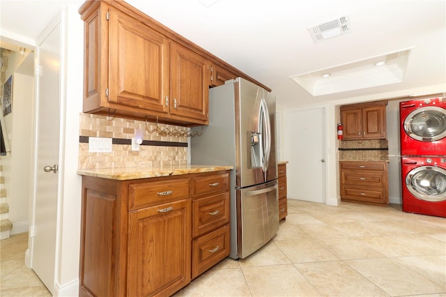 kitchen featuring a raised ceiling, stainless steel fridge, light stone countertops, light tile patterned floors, and stacked washer / drying machine