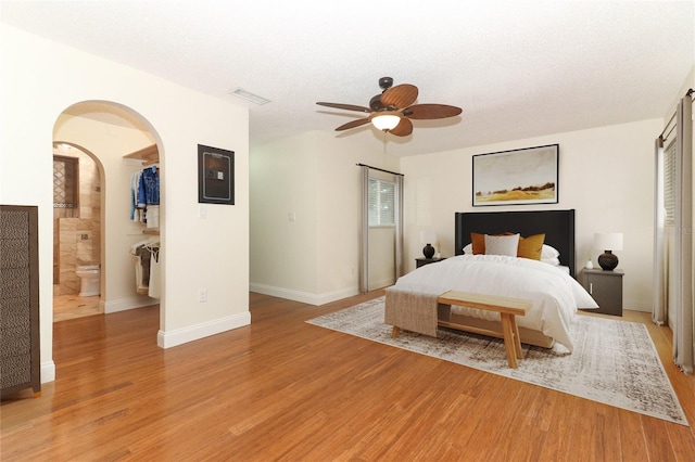 bedroom with a textured ceiling, light hardwood / wood-style flooring, ceiling fan, and connected bathroom