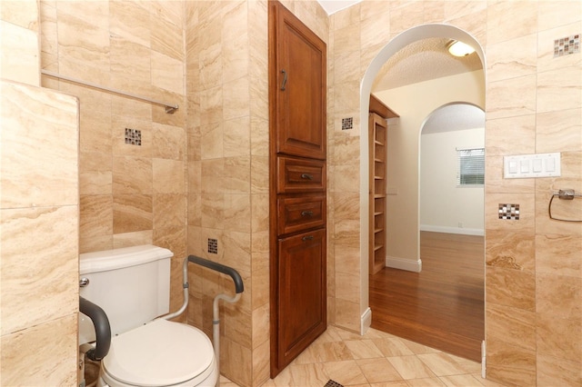 bathroom with hardwood / wood-style floors, toilet, tile walls, and a textured ceiling