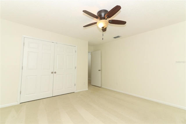 unfurnished bedroom featuring a textured ceiling, a closet, ceiling fan, and light colored carpet