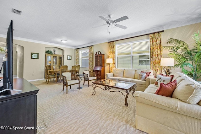 living room featuring light colored carpet, ornamental molding, a textured ceiling, and ceiling fan