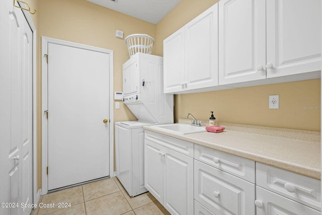 laundry room featuring sink, stacked washer and clothes dryer, light tile patterned floors, and cabinets