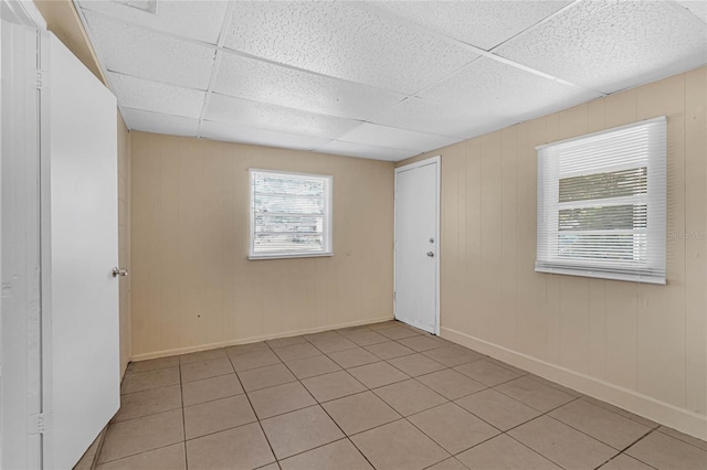 empty room with a paneled ceiling, light tile patterned floors, and wooden walls