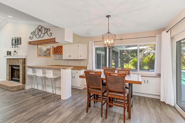 dining area with crown molding, vaulted ceiling, a brick fireplace, a chandelier, and light hardwood / wood-style floors