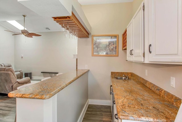 kitchen with kitchen peninsula, white cabinetry, ceiling fan, light stone counters, and dark hardwood / wood-style floors