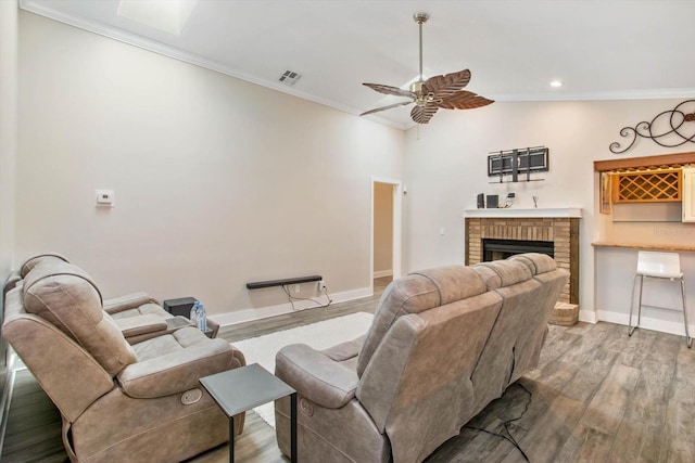 living room with light wood-type flooring, crown molding, a brick fireplace, and ceiling fan