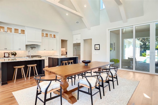 dining room with sink, light hardwood / wood-style floors, high vaulted ceiling, and beam ceiling