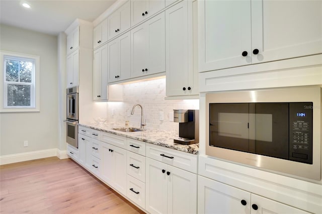 kitchen featuring sink, white cabinetry, light hardwood / wood-style floors, light stone counters, and black microwave