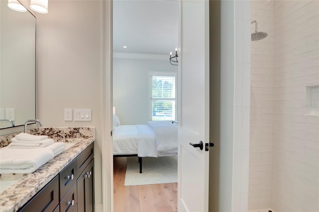 bathroom featuring ornamental molding, hardwood / wood-style floors, an inviting chandelier, vanity, and a tile shower