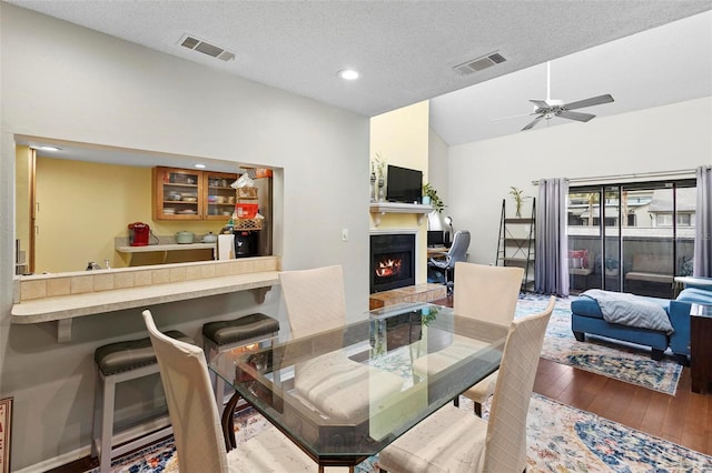 dining area with a textured ceiling, ceiling fan, wood-type flooring, and vaulted ceiling