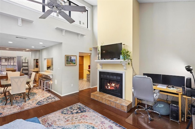 office space with a high ceiling, ceiling fan, a tile fireplace, and dark hardwood / wood-style flooring