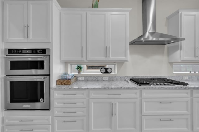 kitchen with white cabinets, wall chimney exhaust hood, light stone countertops, and stainless steel appliances