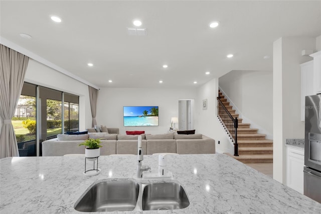 kitchen with stainless steel refrigerator with ice dispenser, white cabinetry, and light stone counters