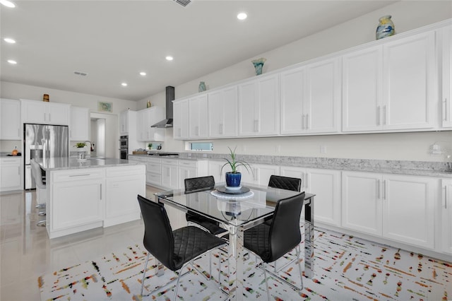 kitchen with appliances with stainless steel finishes, wall chimney exhaust hood, a breakfast bar, white cabinets, and a kitchen island