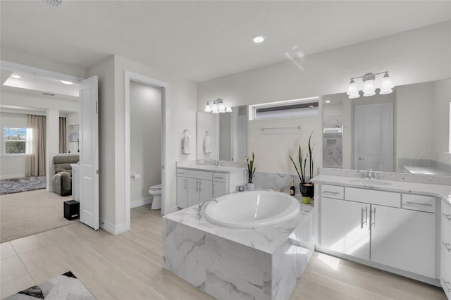 bathroom with tiled bath, vanity, wood-type flooring, and toilet