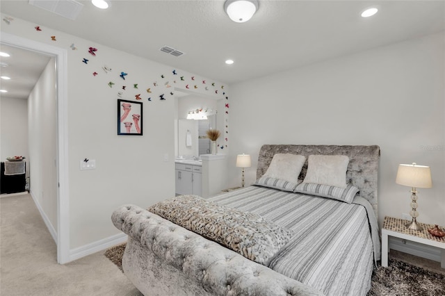 bedroom with ensuite bathroom and light colored carpet