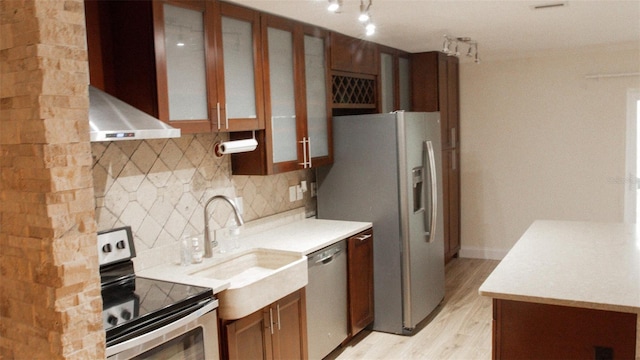 kitchen featuring decorative backsplash, appliances with stainless steel finishes, light hardwood / wood-style flooring, wall chimney exhaust hood, and sink