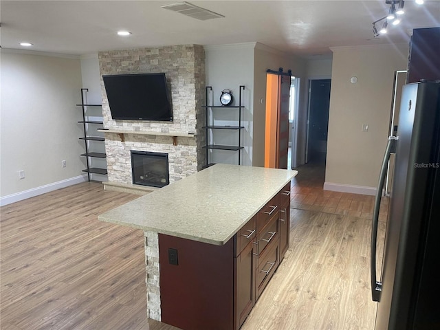 kitchen featuring stainless steel refrigerator, dark brown cabinetry, a kitchen island, a barn door, and light wood-type flooring