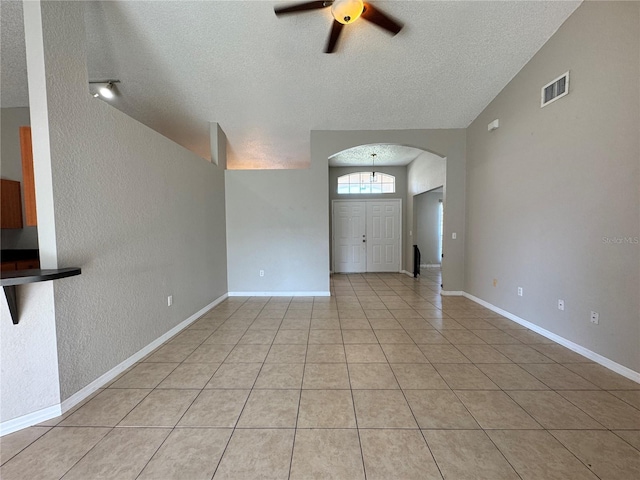 unfurnished living room featuring lofted ceiling, ceiling fan, light tile patterned floors, and a textured ceiling