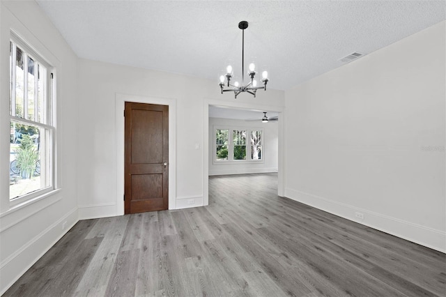 unfurnished dining area featuring wood-type flooring, a textured ceiling, and ceiling fan with notable chandelier