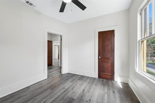 empty room with a wealth of natural light, light wood-type flooring, and ceiling fan with notable chandelier