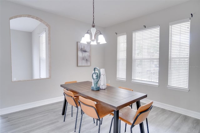 dining area with light wood-style floors, arched walkways, baseboards, and a notable chandelier